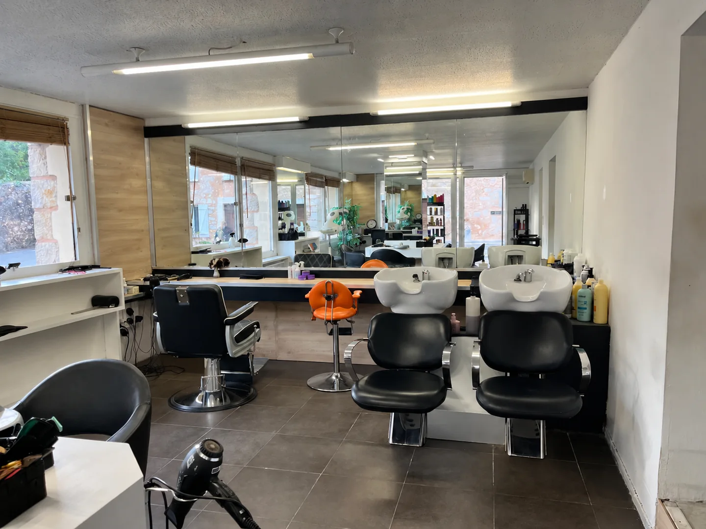 Bacs à shampoing à droite et espace homme / barber à gauche, devant le grand miroir du salon